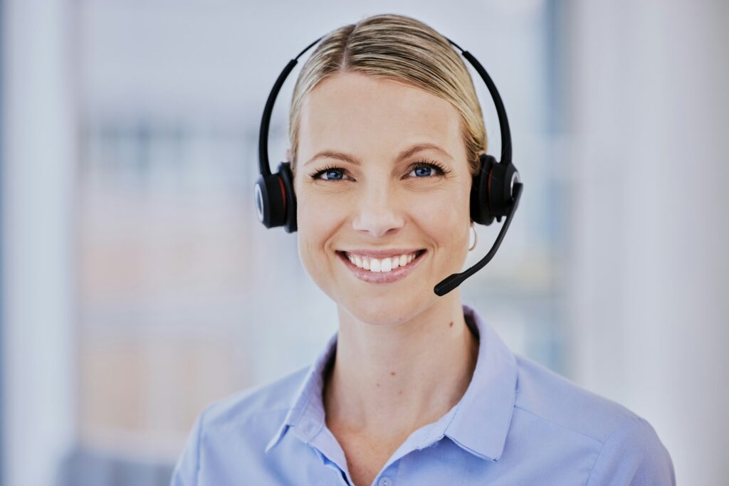 Smiling young caucasian female call centre agent talking on headset while working in an office. Con